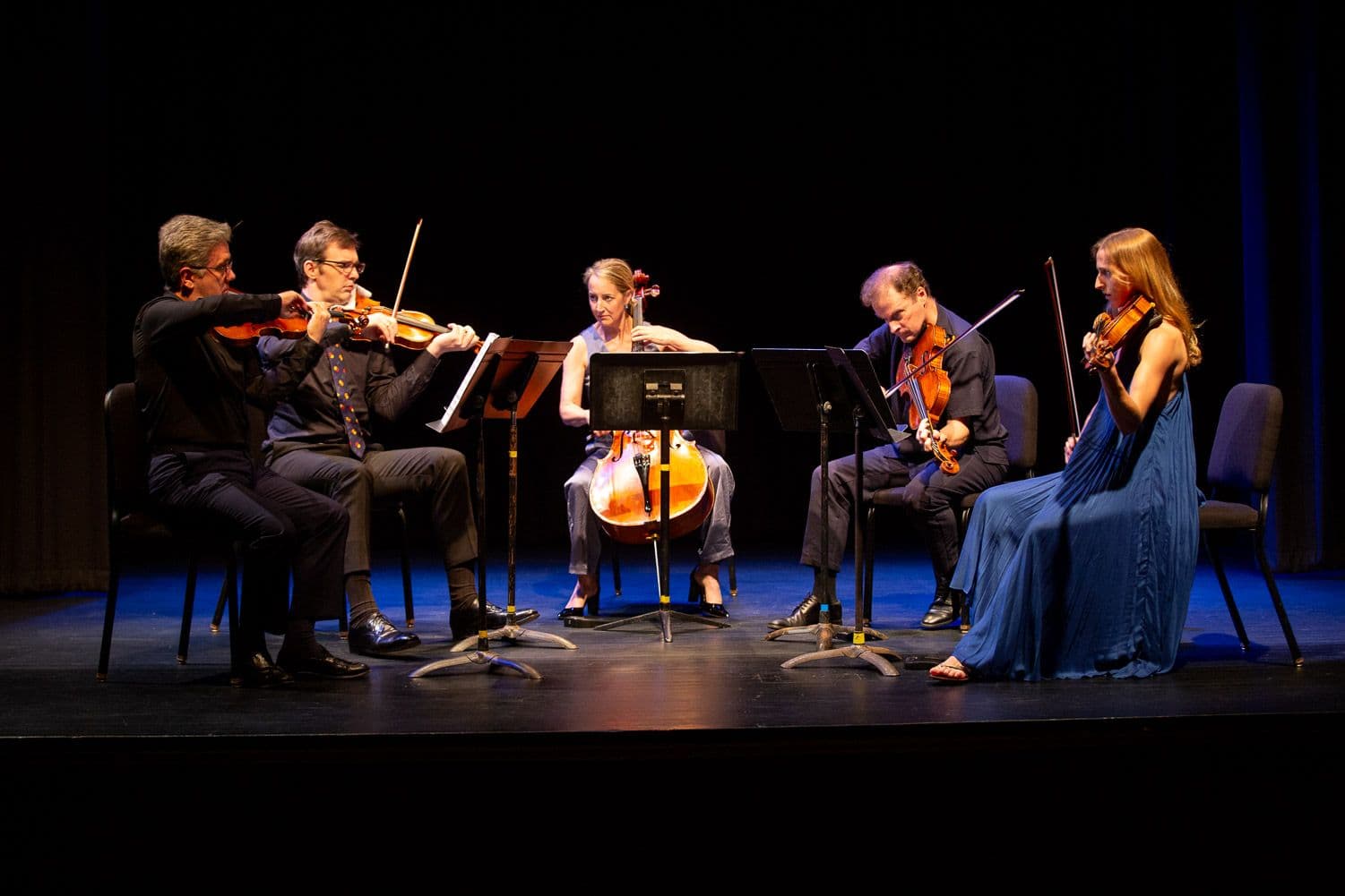 Five orchestral chamber musicians perform in a semi-circle on a black stage
