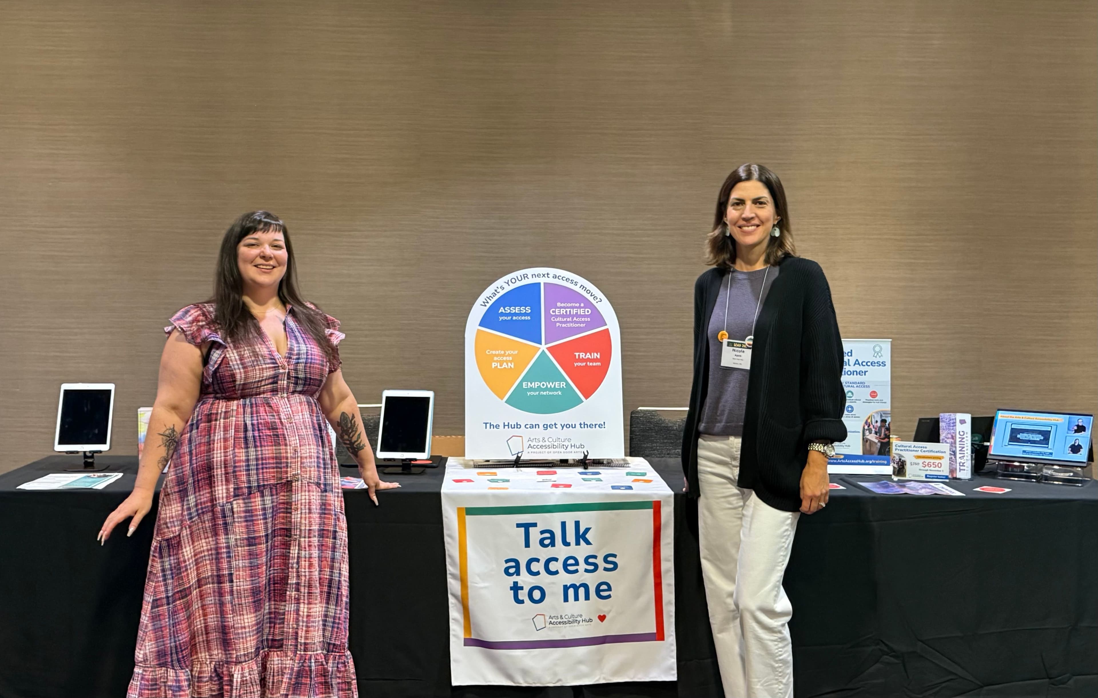 Two people from Open Door Arts stand next to a display about accessibility