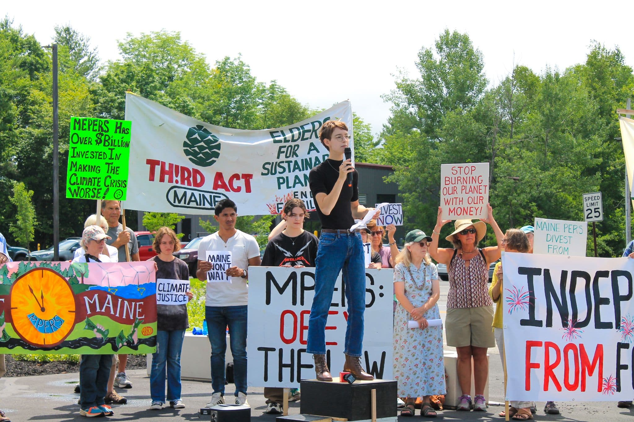 A young climate activist speaks into a microphone among a crowd at a rally